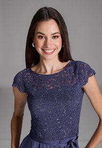 Robe bleu marine avec un corsage en dentelle présentant des motifs floraux complexes et des paillettes, manches courtes et une jupe lisse et fluide avec une ceinture à nouer.