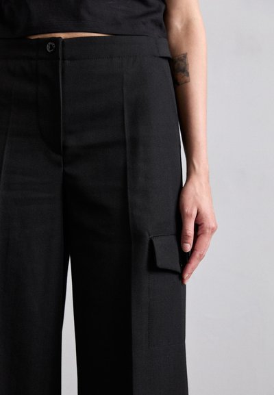 Black wide-leg pants made from smooth fabric, featuring a side cargo pocket and a button closure at the waist.