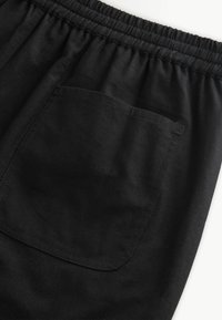 Gros plan sur une ceinture élastique noire avec une poche arrière carrée sur un pantalon en tissu noir.