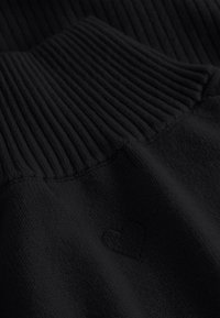 Zwarte trui met geribbelde kraag en zachte textuur. Heeft een subtiele geborduurde hartdetail. De stof lijkt dik en comfortabel.