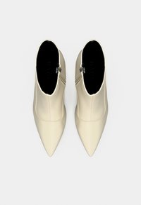 Paire de bottines crème à bout pointu avec fermetures éclair latérales, vues de dessus sur un fond blanc.