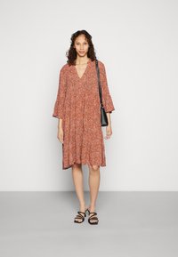 Vestido floral vermelho com mangas de três quartos, decote em V e cintura franzida. Combinado com sandálias pretas de tiras e uma pequena bolsa preta.
