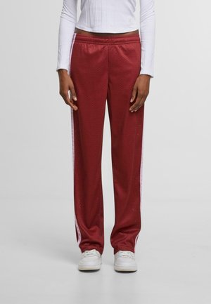 Pantalones deportivos rojos con una superficie texturizada, que cuentan con franjas laterales blancas y una cinturilla elástica, combinados con zapatillas blancas.