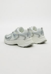 Pareja de zapatillas chunky blancas y plateadas con superposiciones de malla y sintético, suela gruesa y lengüetas en un fondo liso.