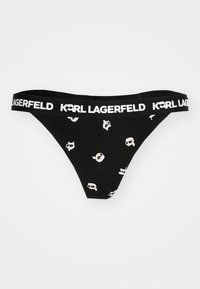 Juodas thong tipo apatinis trikotažas su plačiu baltu juostos kraštu, ant kurio užrašyta "KARL LAGERFELD." Visame paviršiuje puikuojasi žaismingi šviesių spalvų raštai.
