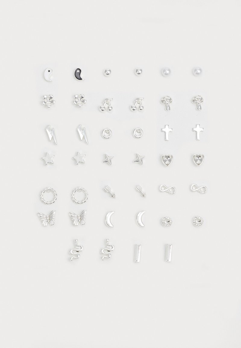 Set aus silbernen Ohrringen mit verschiedenen Formen: Sterne, Herzen, Kreuze und Symbole wie Schlangen und Schmetterlinge, mit einer Mischung aus Texturen und Oberflächen.