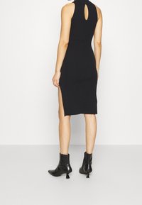 Abito nero in maglia con dettaglio a occhiello sul retro, lungo fino al ginocchio, con spacchi laterali. Abbinato a stivaletti neri e una texture morbida.