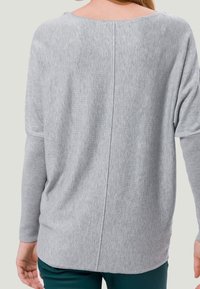 Haut à manches longues gris clair fait en tissu doux, avec un col rond et une couture centrale dans le dos, doté de manches amples.