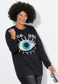 Zwarte sweatshirt met lange mouwen, voorzien van een grote oogafbeelding in blauw en wit, met de tekst "See You" in rhinestones. Celvormige zoom.