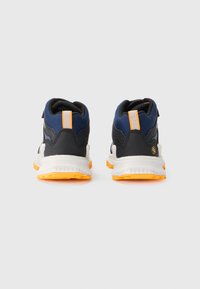 Sneakers featuring a black and navy upper, orange accents, a white midsole, and textured rubber outsole. Adjustable strap for secure fit.