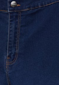 Tela de mezclilla azul oscuro con costuras visibles en color naranja, un botón metálico en la cintura y un bolsillo en el lado derecho. Textura suave.