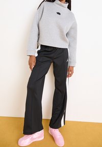 Šedá zkrácená mikina s černým logem, kombinovaná s černými sportovními kalhotami se bílými bočními pruhy a růžovými teniskami.