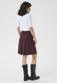 Jupe évasée bordeaux avec taille smockée, associée à des bottes noires jusqu'aux genoux. Le haut est ajusté, blanc et à manches courtes.