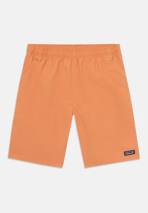 Calções laranja claro feitos de um tecido liso, com uma cintura elástica, costuras planas e um pequeno rótulo de marca perto da bainha.