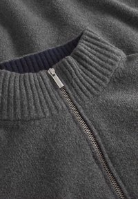 Maglione di lana grigia con colletto a costine e zip argentata. Il colletto interno presenta un costina di un blu scuro a contrasto. Morbido al tatto.