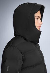 Crna puf jakna s visokim, izoliranim kapuljačom. Ima glatku teksturu i RECCO brendiranje na rukavu. Prednje zatvaranje na rajsferšlus.