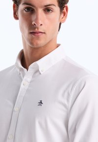 Witte button-up shirt gemaakt van katoen, met een opgevouwen kraag en een klein marineblauw pinguïn-logo op de linkerborst. Glad textuur.