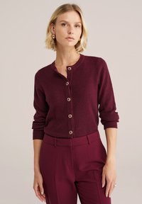 Cardigan bordeaux avec fermeture à boutons, tissu texturé et manches longues. Assorti à un pantalon bordeaux.