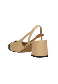 Scarpa slingback in pelle beige con punta rotonda, dettaglio della punta nera, cinturino alla caviglia regolabile e tacco spesso.