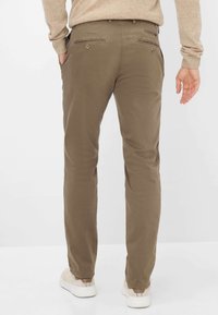 Pantaloni marroni con un design a gamba dritta. Realizzati in tessuto morbido, presentano due tasche posteriori con zip orizzontali. Indossati con sneakers color crema.