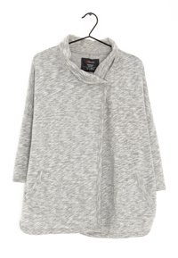 Poncho de felpa gris jaspeado con cuello de chal, mangas de tres cuartos y dos bolsillos frontales. Textura suave con un corte holgado y dobladillo curvado.