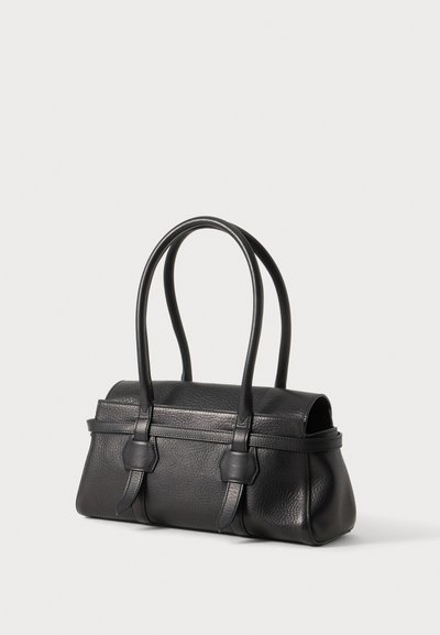 Sac à main en cuir noir texturé avec double poignée supérieure et détails de sangle sur un fond clair uni.