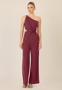 Tuta bordeaux con design a spalla unica, dettaglio intrecciato sul davanti e taglio ampio. Tessuto liscio ed elastico con una leggera lucentezza.