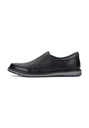 Zapato negro de cuero tipo slip-on con detalles cosidos y suela de goma gris, diseñado para uso casual o formal.