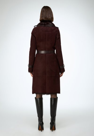 Bordový semišový kabát s kožušinovým golierom, opaskom v páse a dlhými rukávmi, zladiť s elegantnými čiernymi čižmami po kolená. Hladká textúra a prispôsobený strih.