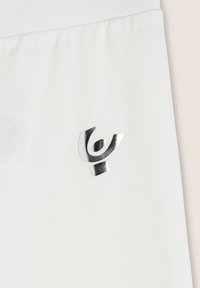 Tessuto bianco con un piccolo emblema astratto color argento lucido, caratterizzato da forme curve e circolari vicino al centro.