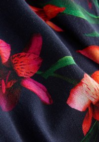 Ziedu audums ar dzīvīgām sarkanām un rozā ziediem uz tumši zila fona. Mīksta tekstūra ar redzamām aušanas detaļām un zaļām lapām.