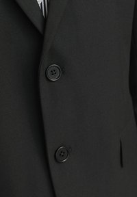 Schwarzer Blazer aus strukturiertem Stoff, ausgestattet mit zwei runden schwarzen Knöpfen und einem Reverskragen. Zu den Details gehören eine taillierte Passform und seitliche Taschen.