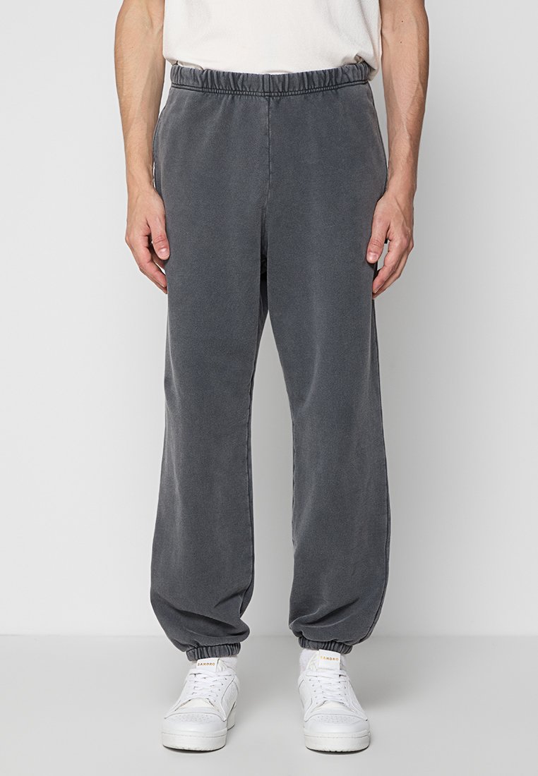 Pantalones de chándal de algodón gris oscuro con cintura elástica, tobillos ajustados y bolsillos laterales. Combinados con zapatillas blancas.