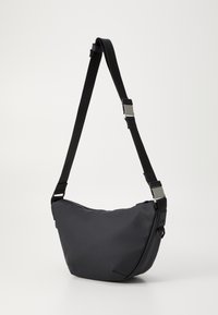 Schwarze Schultertasche mit geschwungener Form, aus strapazierfähigem Stoff gefertigt. Verfügt über einen verstellbaren Riemen und metallische Hardware-Details.
