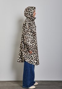 Abrigo de estampado de leopardo con capucha ajustada, bolsillos laterales y una silueta suelta y alargada. Llevado sobre unos vaqueros de pierna ancha azules y zapatillas.