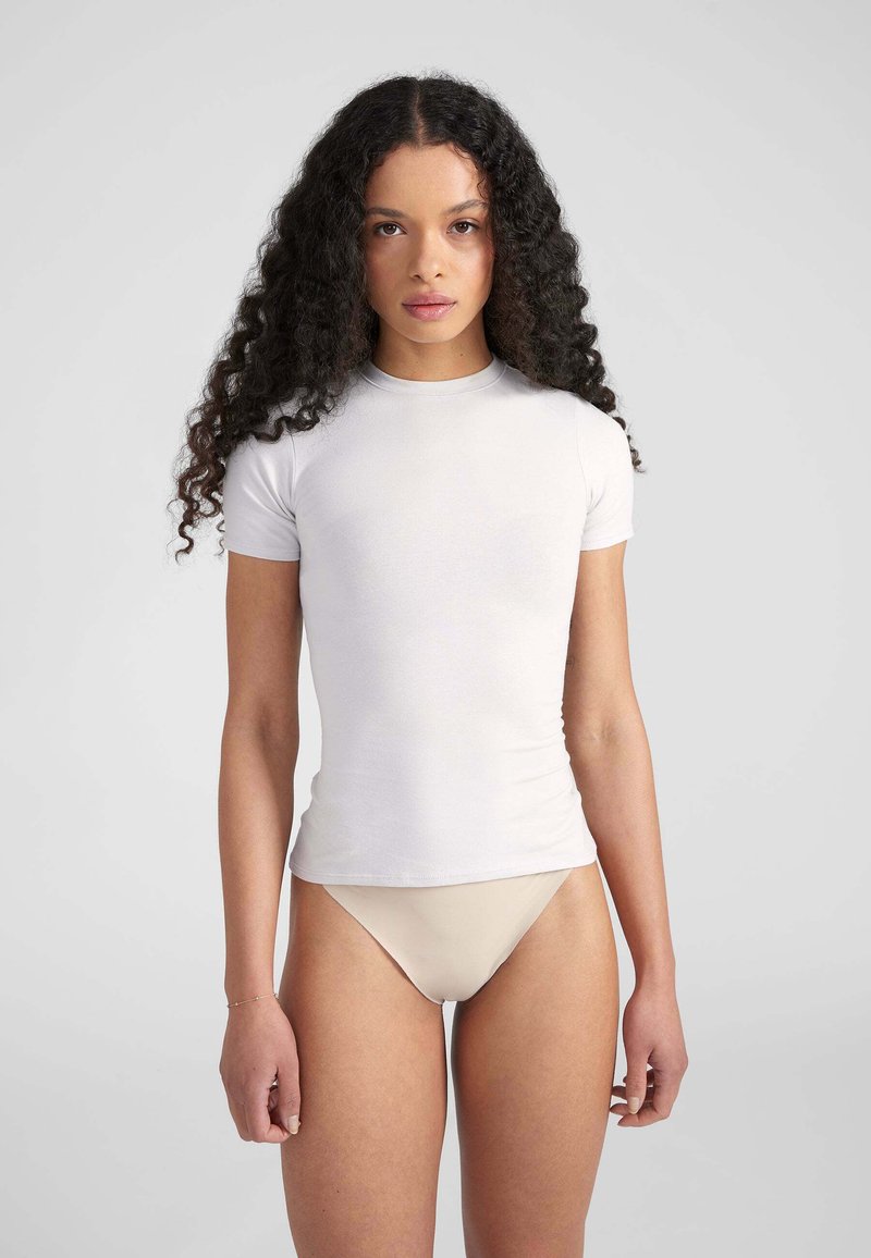 T-shirt fitted bianco a maniche corte con scollo rotondo, realizzato in un tessuto morbido. Sullo sfondo grigio neutro, che mette in risalto il capo.