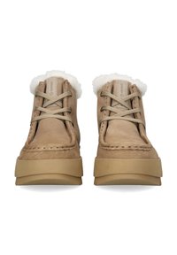 Stivaletti alla caviglia in suede marrone con una soffice fodera bianca, lacci beige e una spessa suola in gomma. Presentano cuciture a vista e accenti con marchio.