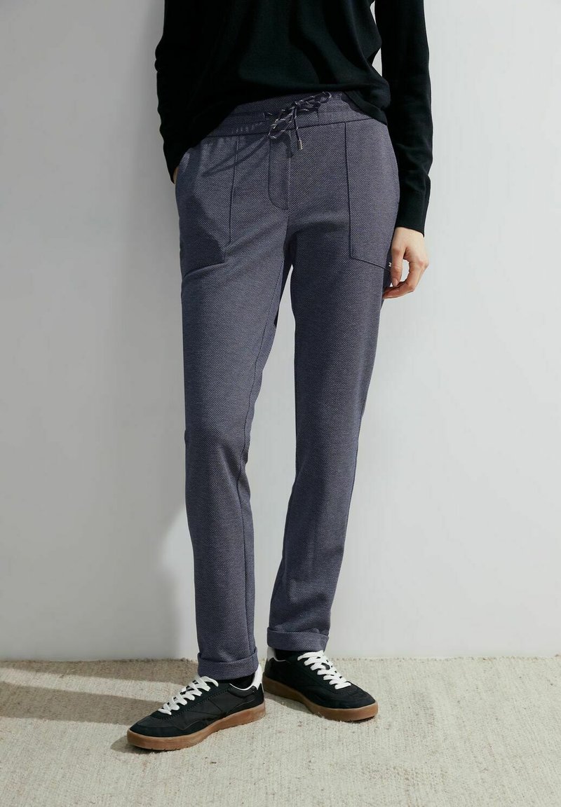 Grå strukturerade sweatpants med dragsko i midjan och två frontfickor, tillsammans med svarta sneakers och en svart långärmad topp.