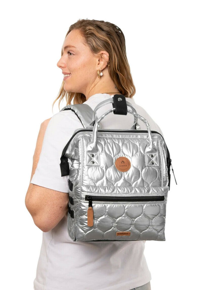 Silberne gepolsterte Rucksack mit doppelten Griffen, externem Reißverschlussfach und braunem Logoakzent. Verfügt über verstellbare Träger und strukturierte Oberfläche.