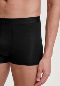 Zwarte herenslips met een zachte, fitted ontwerpen en een elastische tailleband met een gestructureerd logo. Glad stof met minimale naden.