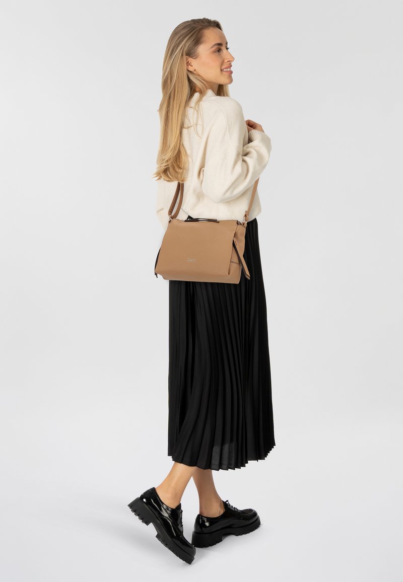 Tasche aus braunem Leder im Querformat mit glatter Textur und Reißverschluss. Ein schwarzer plissierter Rock und glänzende schwarze Schuhe vervollständigen das Outfit.