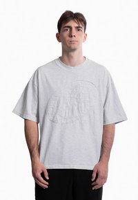 Lys grå oversized T-shirt lavet af bomuld, med et struktureret grafisk design på fronten og en rund halsudskæring. Korte ærmer.