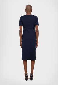 Sötétkék midi ruha rövid ujjakkal, testhez simuló felső résszel és bő szoknyával. Sima szövet textúra, letisztult dizájn, fekete magassarkú cipővel viselve.