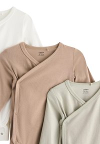 Tre langermede omslag i hvit, beige og lysegrønn bomull, med V-hals-design og trykknapper på sidene.