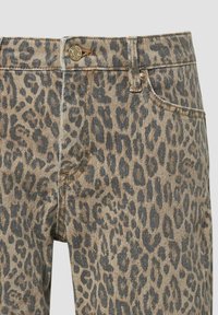 Gros plan d'un jean en denim marron avec imprimé léopard gris foncé et fermeture par bouton métallique à la taille, montrant le détail de la poche avant.