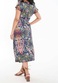 Vue arrière d'une robe à manches courtes à motif floral, avec une base bleue marine ornée de dessins colorés. Portée avec des sandales à talons marron.