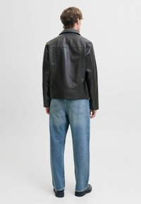Schwarze Lederjacke mit geradem Schnitt, Rückenpasse und langen Ärmeln. Kombiniert mit hellblauen, lässig geschnittenen Jeans.