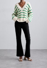 Pull en maille rayée avec décolleté en V en crème et vert, associé à un pantalon noir évasé et des talons ouverts beige. Détail du tissu texturé.