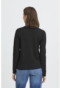 Haut noir à manches longues avec un col rond, fabriqué dans un matériau lisse. Associé à un denim bleu, vue de dos et coupe ajustée.