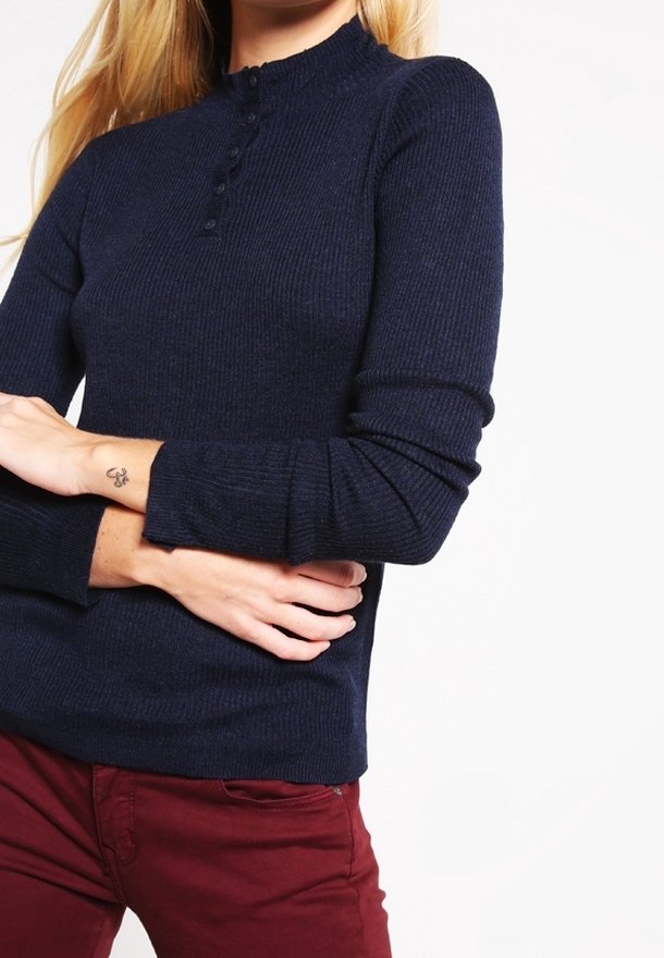 Granatowy sweter z prążkowanego dzianiny z wysokim kołnierzem, detalami z guzikami przy szyi i długimi rękawami, zestawiony z bordowymi spodniami.